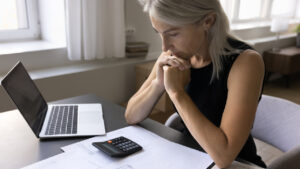 Small business owner reviewing documents with a calculator and laptop, reflecting on how to reduce business expenses and improve financial efficiency.
