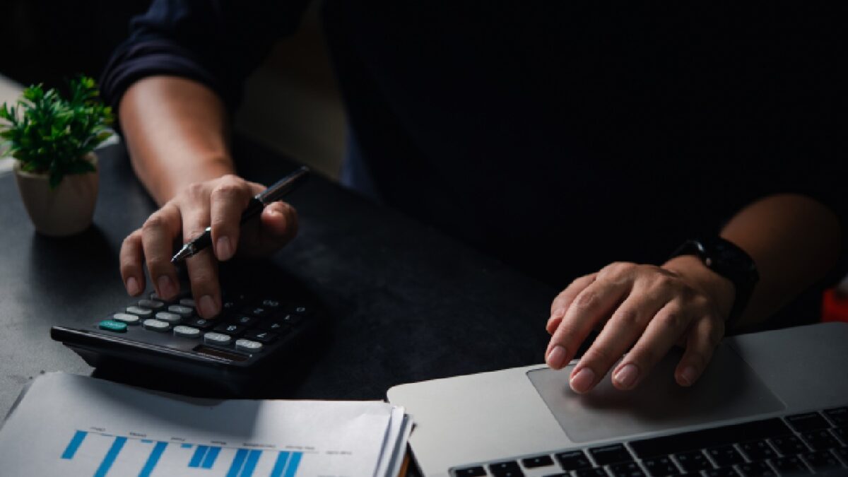 Person working on budgeting for small business with a calculator, laptop, and financial reports on a desk.