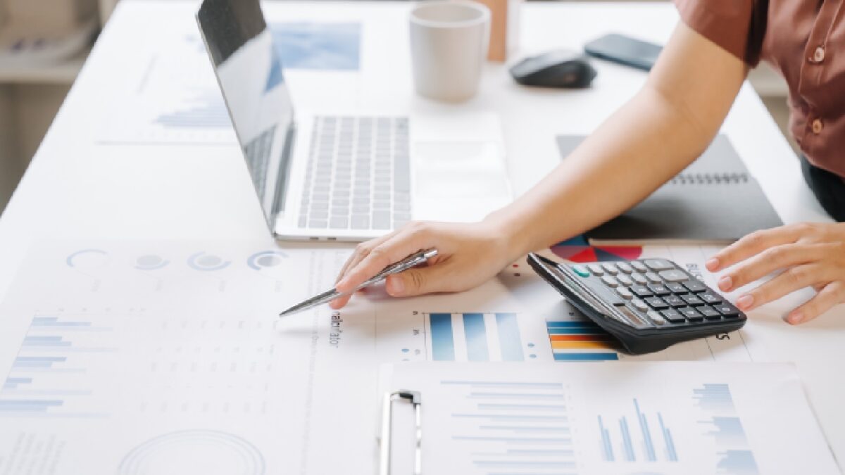 Business owner reviewing a profit and loss report with financial charts, calculator and laptop to analyse business performance and profitability.