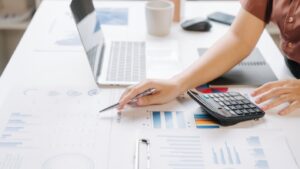 Business owner reviewing a profit and loss report with financial charts, calculator and laptop to analyse business performance and profitability.